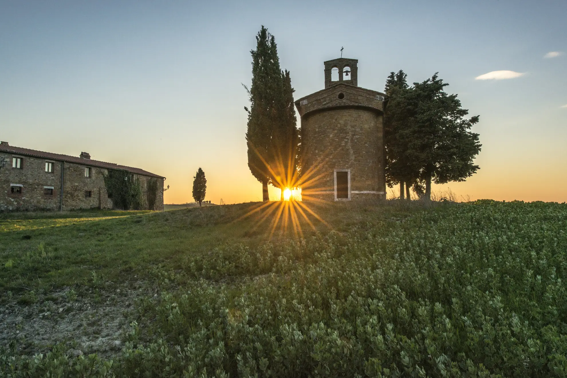 The warm glow of sunset over Cappella Vitaleta in the rolling Tuscan hills.