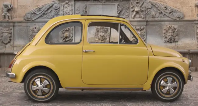 A classic vintage Fiat 500 parked in a scenic Italian setting, symbolising romance and adventure for couples on holiday.