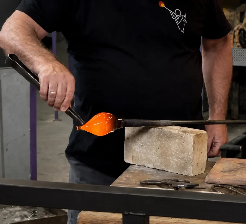 A glassmaker in Murano shaping molten glass on the rod